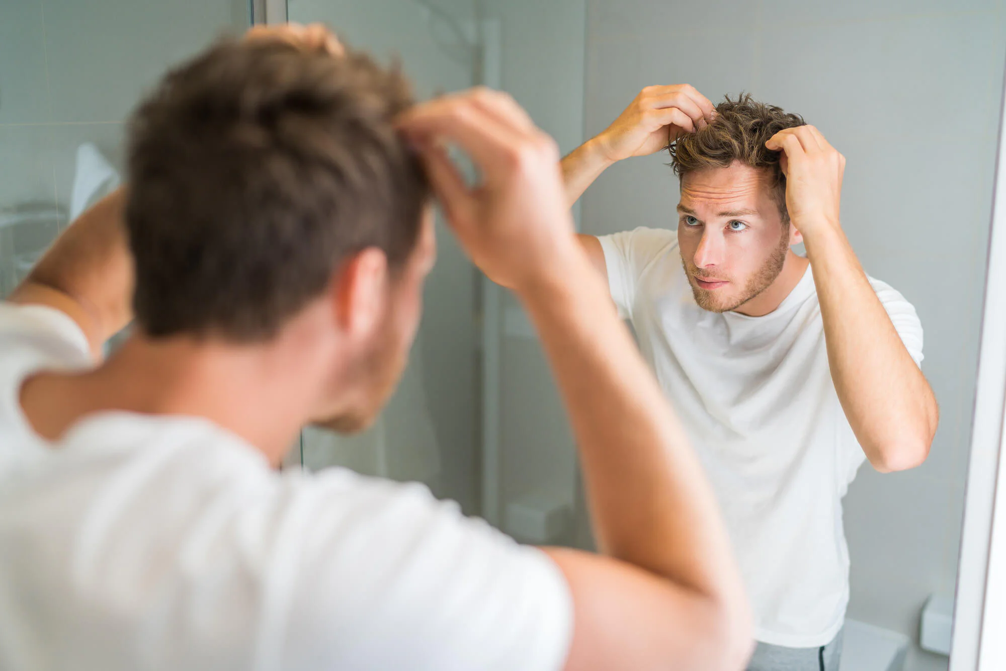 Fit male looking in the mirror styling his hair